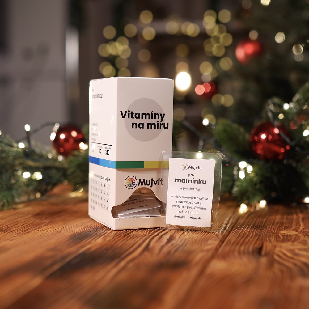 Krabička Vitamíny na míru Mujvit a denní sáček s oslovením pro maminku na dřevěném stole před vánočním stromkem